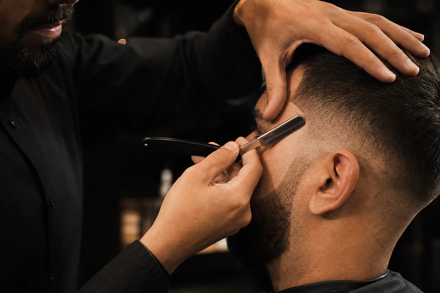 Barbero definiendo con navaja la línea de la sien de un cliente